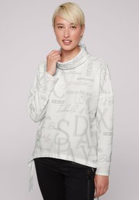 Sudadera de cuello cowl en gris claro con canalé texturizado, que presenta varias frases inspiradoras en colores contrastantes y un detalle de nudo en el costado.