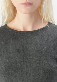 Mørkegrå ribbestrikket topp med rund hals og subtil tekstur. Stoffet viser svake vertikale linjer og en myk overflate.
