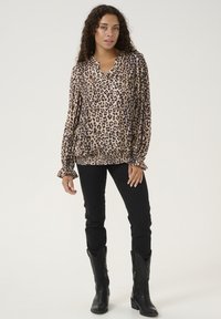 Halenka s leopardím vzorem ve světle béžové a hnědé barvě, s výstřihem do V, dlouhými rukávy s volány, v kombinaci s černými skinny jeans a černými botami.