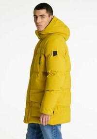 Gul pufferjakke med hætte, der har en frontlynlås, brystlomme og sidelommer. Glat tekstur og ensfarvet, velegnet til vinter.