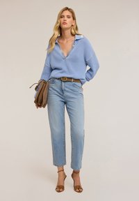 Maglione lavorato a maglia blu chiaro con scollo a V e maniche lunghe, abbinato a jeans blu chiaro a vita media e sandali con tacco marroni. Accento di borsa marrone.