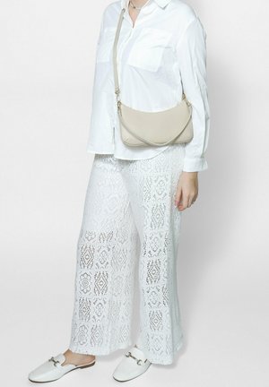Blusa bianca con tasche, abbinata a pantaloni larghi bianchi in pizzo con un motivo geometrico. Borsa a tracolla beige e scarpe bianche senza lacci.