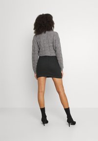 Grå kabelstickad tröja i kombination med en svart minikjol. Svarta ankle boots med klackar. Släta, figurnära texturer och modern silhuett.