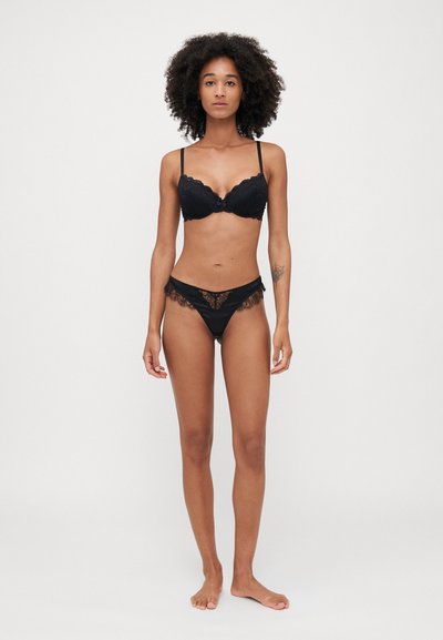 Black lace bra with underwire and scalloped edges, paired with a matching black lace-trimmed thong, displayed on a model.