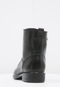 Stivale alla caviglia in pelle nera con una superficie liscia, punta arrotondata e tacco basso impilato. Presenta una lunga linguetta e dettagli di cucitura sottili.