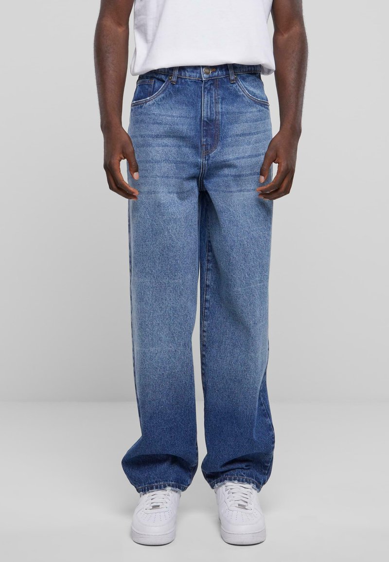 Blå denimjeans med avslappnad passform, hög midja och femficksdesign. Tyget har ljusa blekningar och är parat med vita sneakers.
