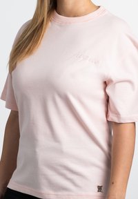 Lyserød kortærmet t-shirt lavet af blød bomuld, med en ribbet rund hals og et subtilt broderet logo på brystet. Sølvfarvet hardware detaljer.