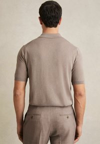 Beige polo-paita lyhythihaisena, valmistettu kevyestä kankaasta, jossa on klassinen kaulus ja sovitettu malli, yhdistettynä vaaleanruskeisiin housuihin.