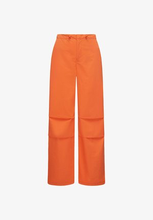 Plati kelnės iš lygios, oranžinės medžiagos. Yra su raišteliu reguliuojamu juosmeniu ir dviem didelėmis siūtomis kišenėmis šonuose.