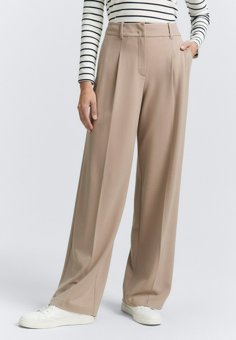 Beige wide-leg trousers with a pleated front, made of smooth fabric. Features side pockets and a relaxed fit, paired with white sneakers.