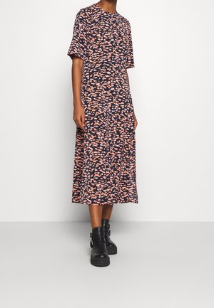 Mujer con un vestido midi de manga corta y un patrón abstracto en rosa y negro, combinado con botas negras de tobillo con hebillas.