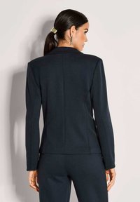 Maßgeschneiderter marineblauer Blazer mit langen Ärmeln, einem Reverskragen und einem strukturierten Schnitt. Glatte Textur mit minimalen Details.