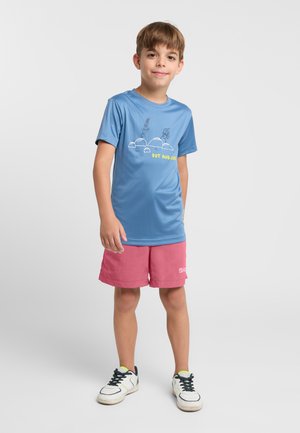 Blaues T-Shirt mit kurzen Ärmeln und grafischem Design, kombiniert mit rosa Shorts. Sneaker mit weißen und schwarzen Akzenten runden das Outfit ab.