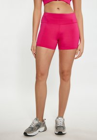 Pangeklede roze sportshorts met een hoge tailleband, een gladde textuur en contrasterende stiksels, gecombineerd met grijze sneakers met witte veters.