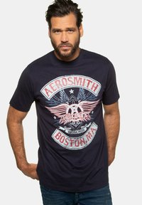 Námorně modré bavlněné tričko s grafickým potiskem křídel a textem: "Aerosmith Boston, MA" v červené a bílé barvě. Krátké rukávy, klasický kulatý výstřih.