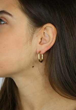 Złota kolczyk-koło o polerowanym wykończeniu, z zaokrąglonym kształtem i zamknięciem na zawiasie, pokazany na uchu modela.