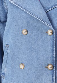 Chaqueta de mezclilla de color azul claro con un diseño de doble botonadura. Presenta grandes botones beige, cuello con muescas y detalles de costura visibles.