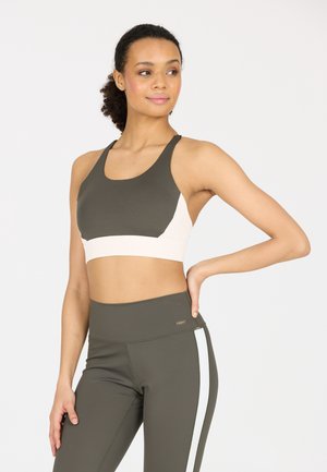 Sostenedor deportivo en verde oliva oscuro con un panel crema; presenta un diseño de espalda nadadora. Leggings altos de cintura en oliva con una franja lateral blanca.