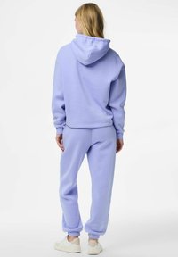 Sada světle fialové mikiny a kalhot z měkké látky. Mikina má velkou kapuci a žebrované manžety; kalhoty mají elastické lemy a přiléhavý střih.