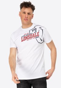 Balta medvilnės marškinėliai su juoda liūto grafika ir raudonu užrašu "LONSDALE". Trumpomis rankovėmis ir apvalia iškirpte.