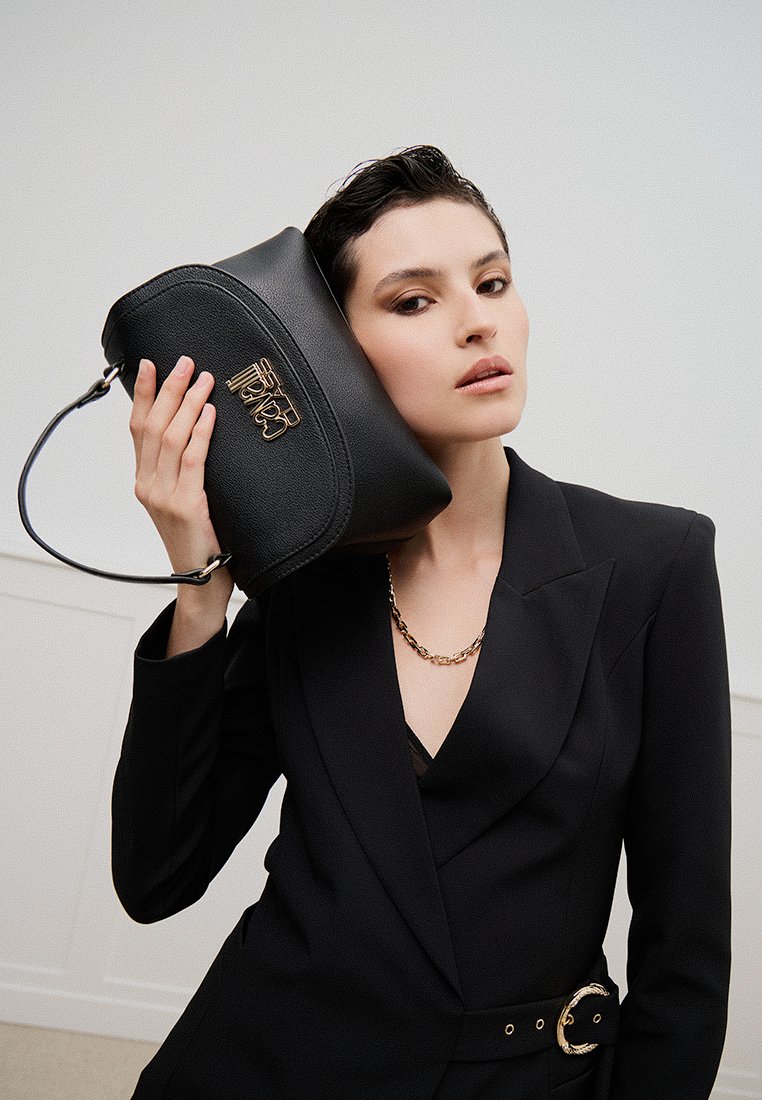 Sac à main en cuir noir avec une forme arrondie, doté d'un logo doré et d'une bandoulière en chaîne. Texture lisse avec des détails de conception minimalistes.