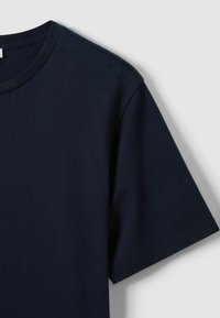 Lihtne tumelõhnaline tumesinine lühikeste varrukatega T-särk kaelusega, nähtav heleda halli tausta ees.