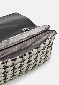 Petit sac bandoulière avec motif pied-de-poule noir et blanc, rabat ouvert et intérieur en tissu gris clair avec un motif circulaire à points.