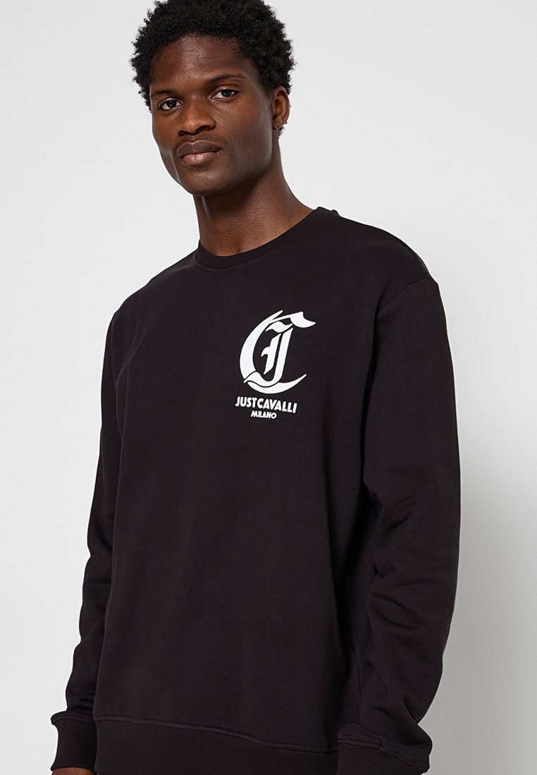 Czarny sweatshirt z okrągłym dekoltem, wykonany z miękkiego materiału. Posiada białe logo "JUST CAVALLI MILANO" na piersi oraz ściągacze na rękawach i u dołu.