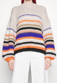 Pull tricoté avec rayures horizontales beige, orange, bleu, noir et vert. Coupe ample avec manches larges et poignets côtelés.