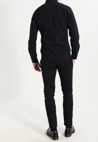 Černá džínová košile s knoflíky a přiléhavým střihem, dlouhými rukávy a kontrastním švem, nošena s černými slim-fit kalhotami a černými botami.