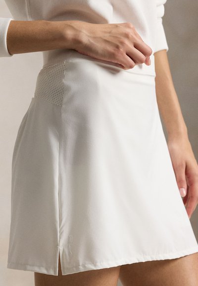 Λευκή αθλητική φούστα με μαλακό ύφασμα, πλαϊνή σκίση και υφασμάτινη λεπτομέρεια στη μέση, με μικρό λογότυπο κοντά στο κάτω μέρος.