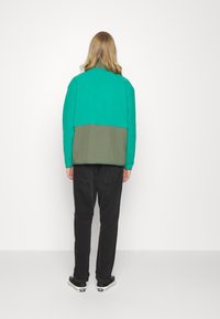 Dwukolorowa bluza w odcieniach zieleni i oliwkowego z luźnym krojem, z wysokim kołnierzem i długimi rękawami, w zestawie z czarnymi jeansami i trampkami.