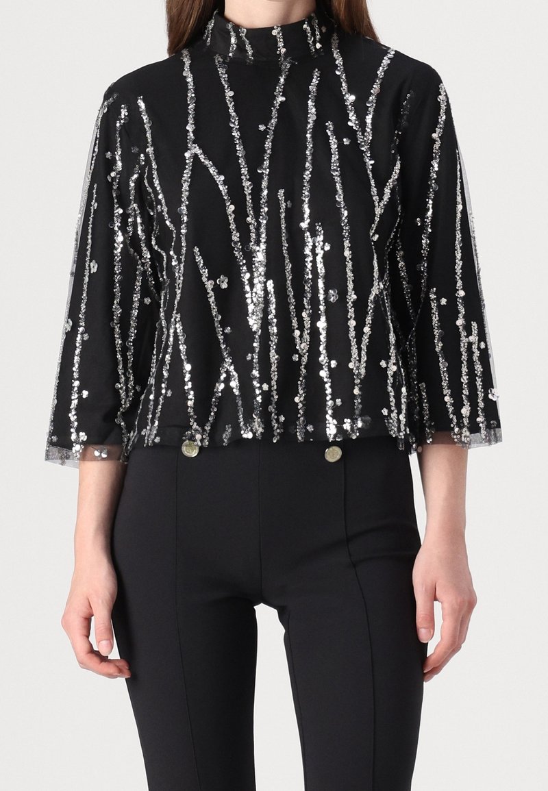 Sort paliettop med trekvartærmer, der har lodrette sølvpalietstriber. Høj halsudskæring, cropped design, glat tekstur.
