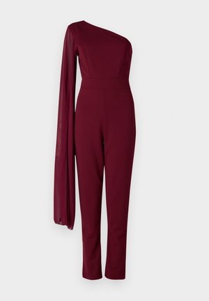 Salopetă burgundy cu un design asimetric pe un umăr. Mânecă lungă, transparentă, talie ajustată și picioare conice, realizate dintr-un material neted.
