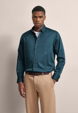 Teal button-down shirt with long sleeves and a collar, paired with light khaki trousers and a brown belt, featuring a smooth fabric texture.