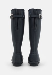 Botas de lluvia de goma negras con acabado texturizado, hebilla lateral ajustable y diseño contorneado. Caña alta con tacón reforzado para mayor estabilidad.