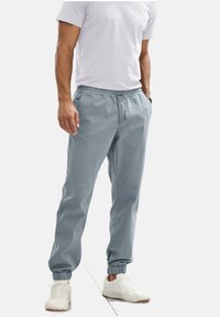 Lichtblauwe katoenen joggers met een elastische tailleband, trekkoord en boorden, gecombineerd met een plain witte t-shirt en witte sneakers.