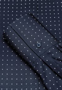 Marineblaues Hemd mit weißen Polka-Dots, glatter Textur und Knopfmanschette. Zeigt einen ordentlich gefalteten Kragen und das Stoffmuster.