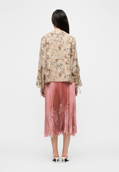 Ελαφριά μπλούζα μακριάς μανίκας σε μπεζ χρώμα με floral εμπριμέ, συνδυασμένη με πλισέ, ροζ φούστα μέχρι το γόνατο, με διαβάθμιση χρωμάτων και λεπτές λουλουδένιες λεπτομέρειες.