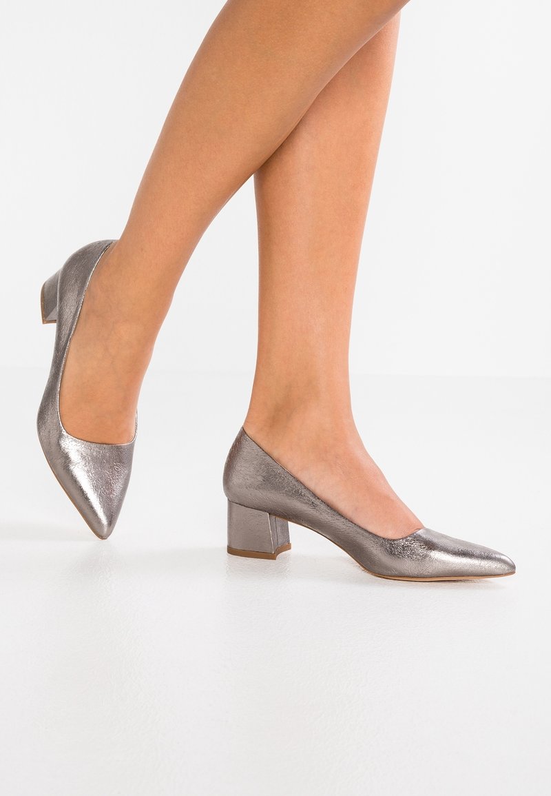 Chaussures à talons en cuir argent métallisé avec un design à bout pointu et un talon carré. Texture lisse, silhouette élégante et style minimaliste.