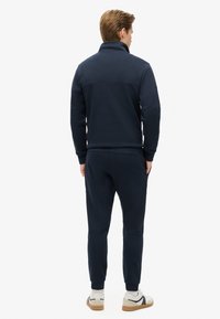 Navyblaues Zip-Jacken-Fleece mit hohem Kragen, weicher Textur, elastischen Bündchen und passenden Jogginghosen mit Seitentaschen.