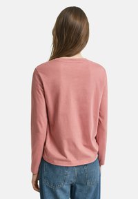 Langärmliges rosa Oberteil aus weicher Baumwolle, mit rundem Ausschnitt und lässiger Passform, kombiniert mit hochtaillierten blauen Jeans.
