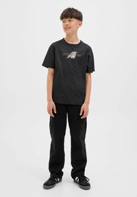 Zwarte katoenen t-shirt met een grafisch logo, gecombineerd met zwarte cargobroeken met zijkanten zakken en gedragen met zwarte sneakers.