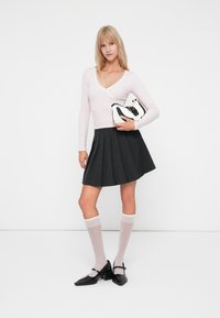 Maglietta a maniche lunghe rosa chiaro con bordo in pizzo, gonna nera plissettata, calze trasparenti fino al ginocchio e scarpe Mary Jane nere in vernice, che tiene una borsa.