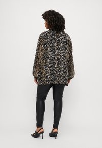Chemisier à imprimé léopard avec des manches amples, leggings noirs et talons ouverts. Le chemisier présente un tissu doux et des motifs contrastés de couleurs foncées et claires.
