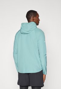 Světle modrá hoodie bunda vyrobená z lehkého materiálu, s měkkou texturou, dlouhými rukávy a mírně křivým lemem.
