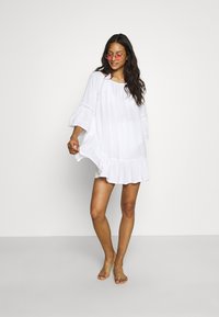 Vestido blanco hasta la rodilla con un dobladillo con volantes, mangas de campana de tres cuartos y detalles de encaje en el escote y las mangas.