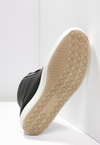 Schwarze Ledersneaker mit weißer Gummisohle. Die Sohle verfügt über ein kreisförmiges Griffmuster. Die Seite hat ein Reißverschlussdetail für ein einfaches Anziehen.