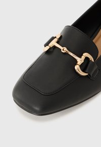 Black leather loafers with a gold-tone hardware accent, square toe design, and flat sole. Smooth texture with visible stitching details.