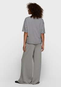T-shirt oversize gris à épaules tombantes, associé à un pantalon gris à jambes larges. Les deux vêtements ont une texture douce et lisse.